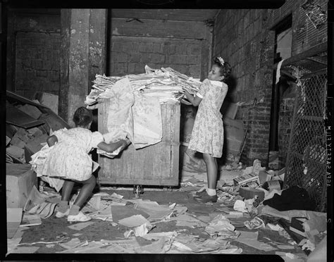 Two Girls Gathering Newspapers On Top Of Box In Interior With Debris