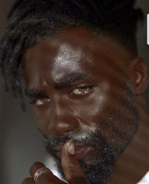 A Man With Dreadlocks Is Holding His Finger To His Mouth And Looking At