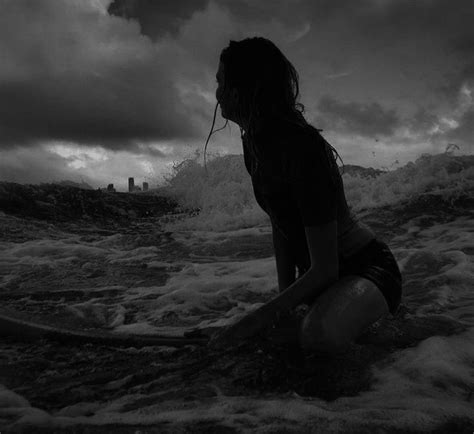 a woman kneeling down in the water with a surfboard under her arm and head