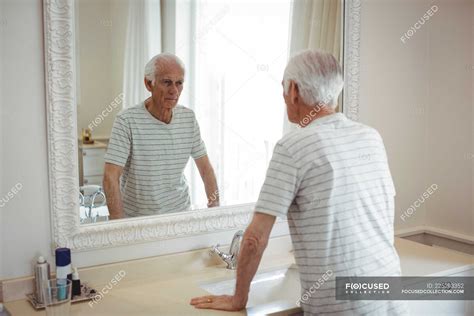 Senior Man Looking At Mirror In Bathroom — Standing Home Stock Photo