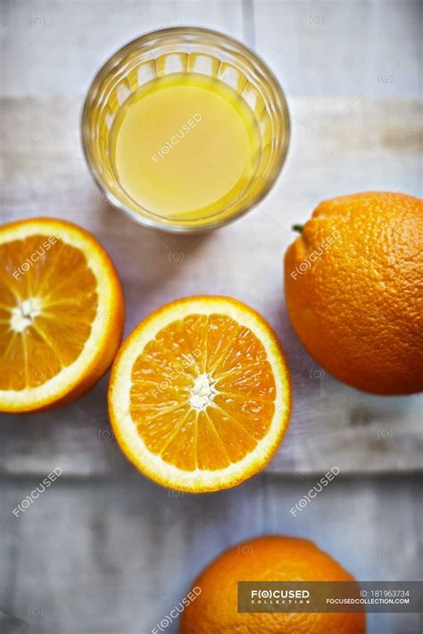 Close Up Of Halved And Whole Oranges And Glass Of Orange Juice On Cloth