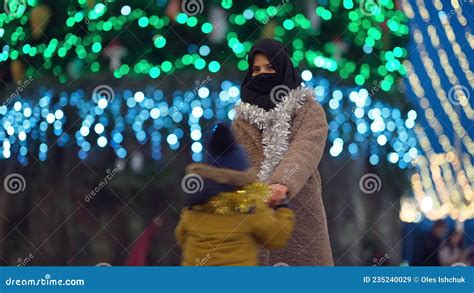 Carefree Excited Middle Eastern Mother And Son Spinning In City With Christmas Lights At