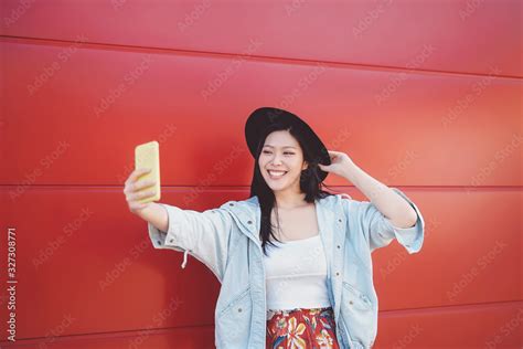 happy asian girl taking selfie with mobile smart phone outdoor trendy influencer having fun