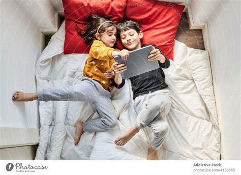 Friendly Siblings Using Tablet Together On Blanket A Royalty Free