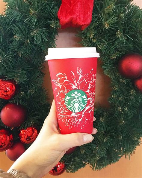 A Starbucks Cup Is Being Held In Front Of A Wreath With Ornaments