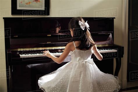 Rear View Of Young Girl Playing Piano In White Dress Stock Photo