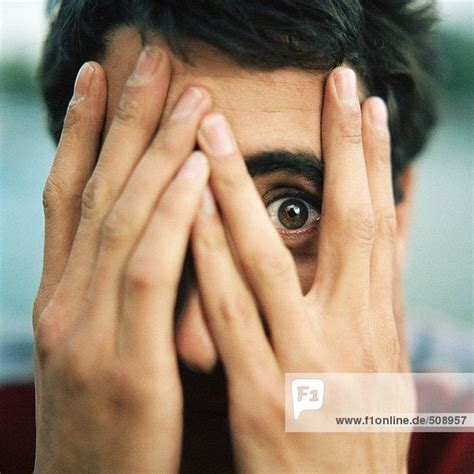 Young Man With Hands Over Face Looking Through Fingers With One Eye