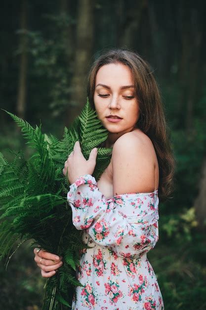 premium photo a cute girl in a floral dress is sitting with a fern bouquet in the forest