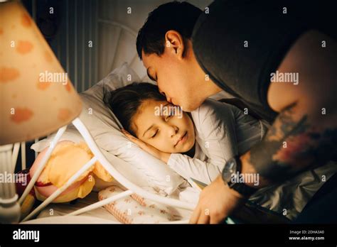 Padre Besando A Su Hija Mientras Duerme En La Cama En Casa Fotografía