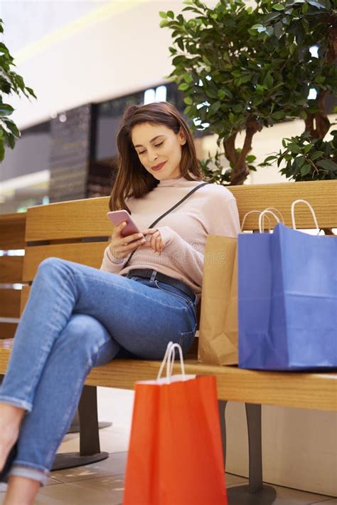 Woman Using Mobile Phone After Big Shopping In Shopping Mall Stock