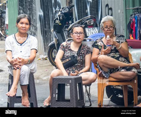 Three Vietnamese Women Sitting On Plastic Chairs On The Pavement