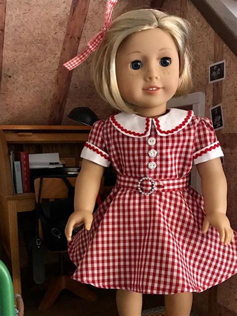 A Doll With Blonde Hair Wearing A Red And White Checkered Dress Standing Next To A Green Chair