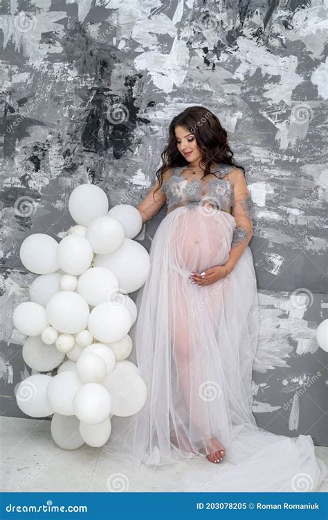 Beautiful Pregnant Woman In Transparent Dress Posing In Studio On Grey