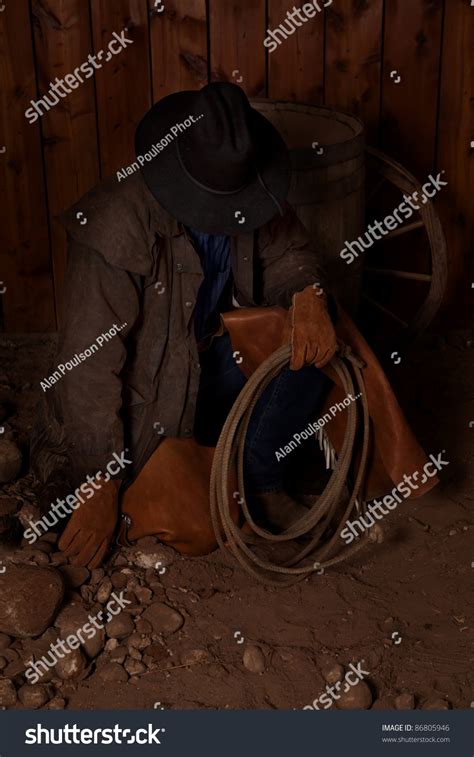 A Cowboy Kneeling Down In The Dirt Looking Down At The Rocks Stock