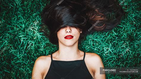 cheerful brunette woman lying in grass with lock of hair over eyes — glamour attractive stock