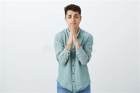 Studio Shot Of Upset Cute European Guy In Shirt Holding Hands In Pray