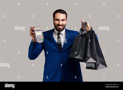 Satisfied Businessman Holding Payment Terminal And Paper Shopping Bags