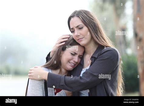 Sad Woman Crying And A Friend Comforting Her Standing In A Park A Foggy