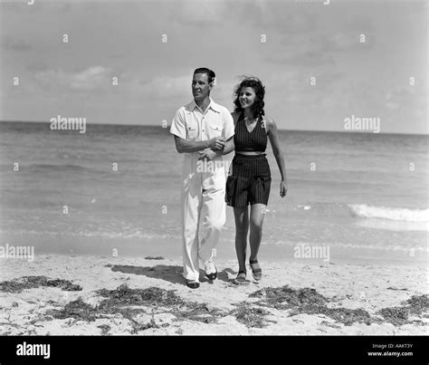 1930s Couple Arm In Arm Walking Up From Ocean Smiling Man In White Shirt And Slacks Woman In Dark
