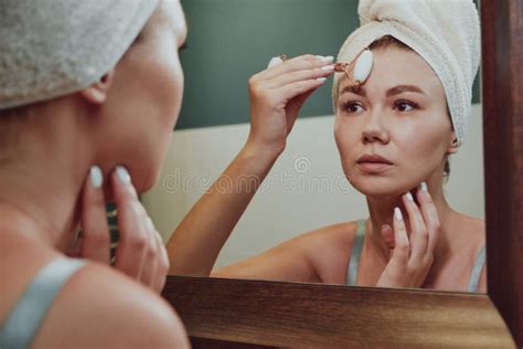 Close Up Woman Using Jade Facial Roller For Face Massage Looking In The Bathroom Mirror Stock
