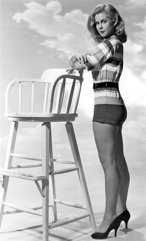 A Woman Standing Next To A Chair With Her Leg On The Back Of A Chair