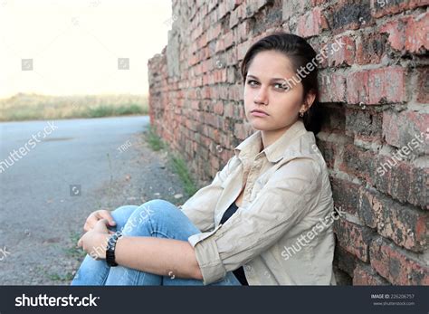 Sad Young Girl Sitting Against A Brick Wall Stock Photo 226206757