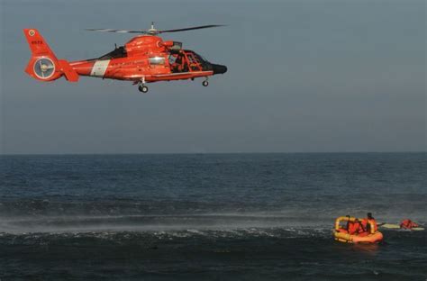 A Red Helicopter Flying Over The Ocean With People In Life Rafts On The