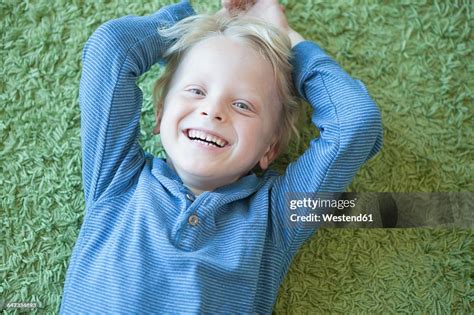 Portrait Of Happy Little Blond Boy Lying On Green Carpet High Res Stock