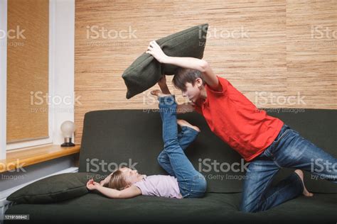 Siblings Having Pillow Fight On A Couch Confined At Home During