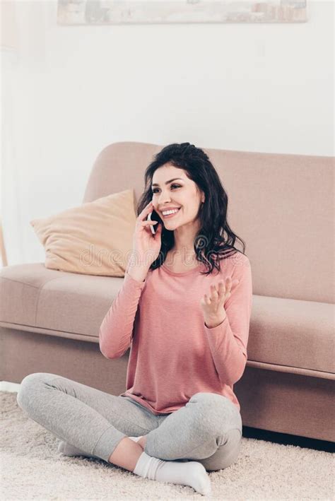 hermosa mujer sonriente sentada en la alfombra hablando en el smartphone y haciendo gestos en
