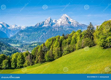 Idyllic Alpine Landscape With Green Meadows Farmhouses And Snowy