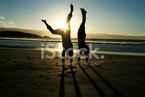 Silhouette Of Two Women Doing Handstand On Beach At Sunset Stock Photo