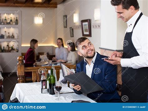 Positive Waiter Taking Order In Restaurant Helping Young Male Stock