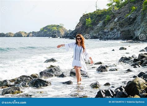 One Redhead Beautiful Girl Walks Barefoot On The Rocks On The Beach