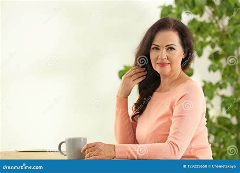 Portrait Of Beautiful Older Woman Sitting At Table Indoors Stock Photo