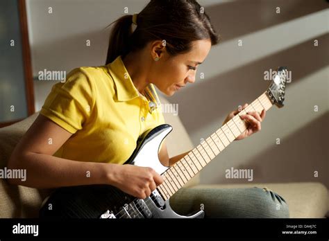 Beautiful Mid Adult Woman Playing Electric Guitar At Home Sitting On