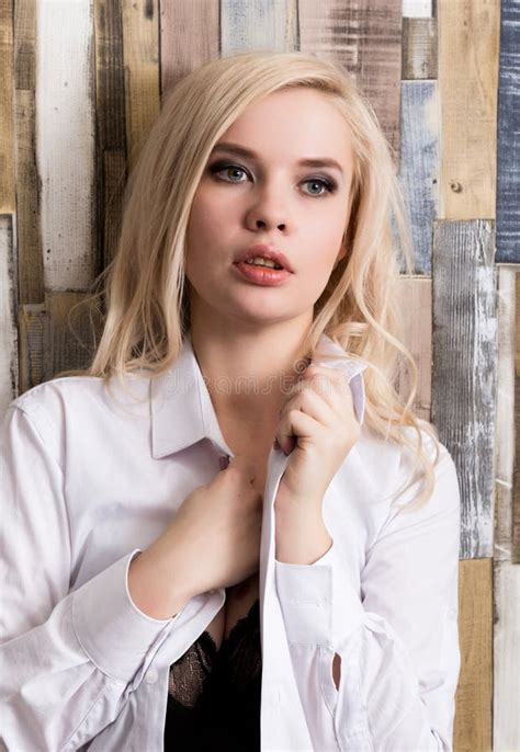 Portrait De La Fille Blonde Attirante Se Tenant Sur Le Fond En Bois De Mur Elle A Des Yeux Bleus