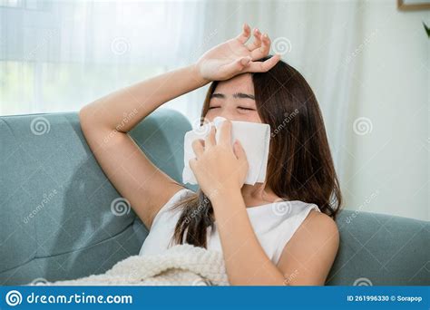 Sick Woman Sitting Under Blanket On Sofa And Sneeze With Tissue Paper