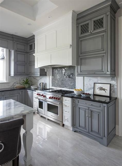 A white island sits atop maple wood bases and houses the cooktop. White Kitchen Hood with Dark Gray Mosaic Cooktop ...