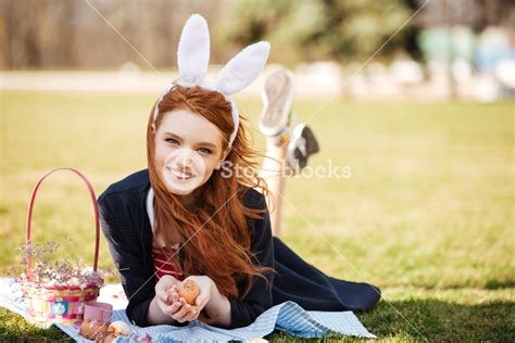 portrait of a smiling happy red head girl wearing easter bunny ears and laying on a grass with