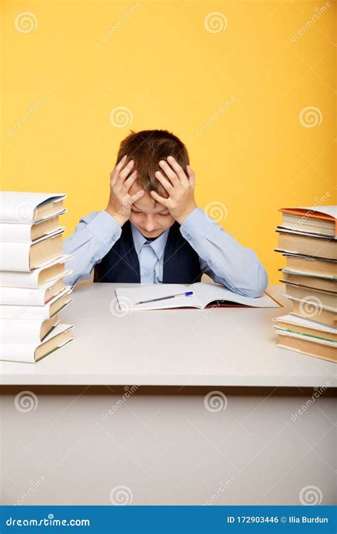 Tired School Boy Sitting At The Desk And Studying Alone Stock Photo