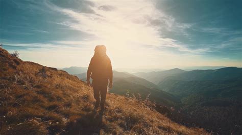 The Male Walking Along The Mountain On The Bright Sunset Background