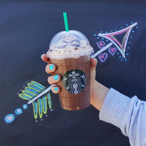 A Woman Holding Up A Starbucks Drink In Front Of A Chalkboard With