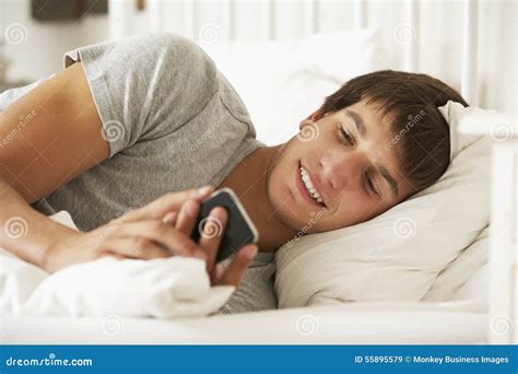 Tiener In Bed Thuis Texting Op Mobiele Telefoon Stock Afbeelding