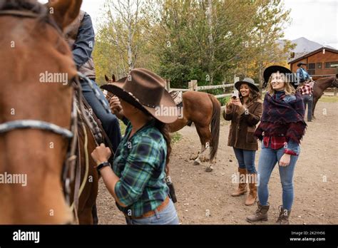 Young Women Watching Friend Mount Horse For Horseback Riding Stock