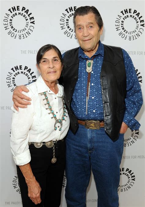 An Older Man And Woman Standing Next To Each Other In Front Of A White Wall