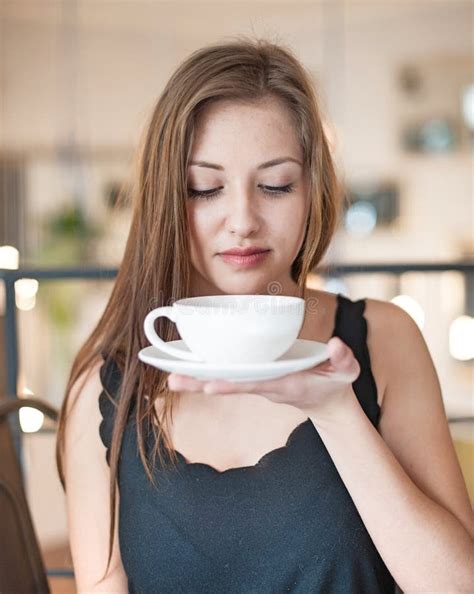 Thoughtful Young Woman Looking Out From Window While Drinking Coffee In
