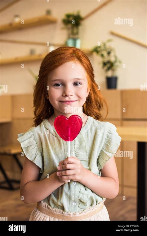 Beautiful Redhead Girl Eating Heart Shaped Lollipop And Looking At Camera Stock Photo Alamy