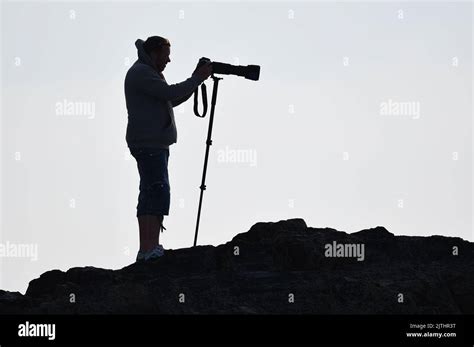 Photographer In Silhouette With Camera And Monopod On Cliffs Stock