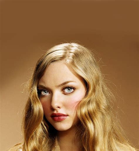 a woman with long blonde hair and blue eyes posing for a photo in front of a brown background